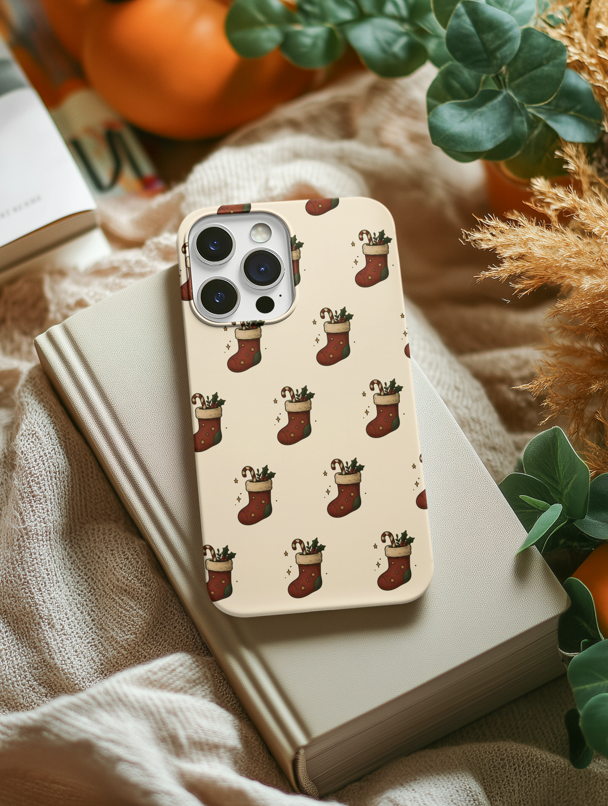 Phone case with Christmas stocking pattern on a surface with pumpkins and plants